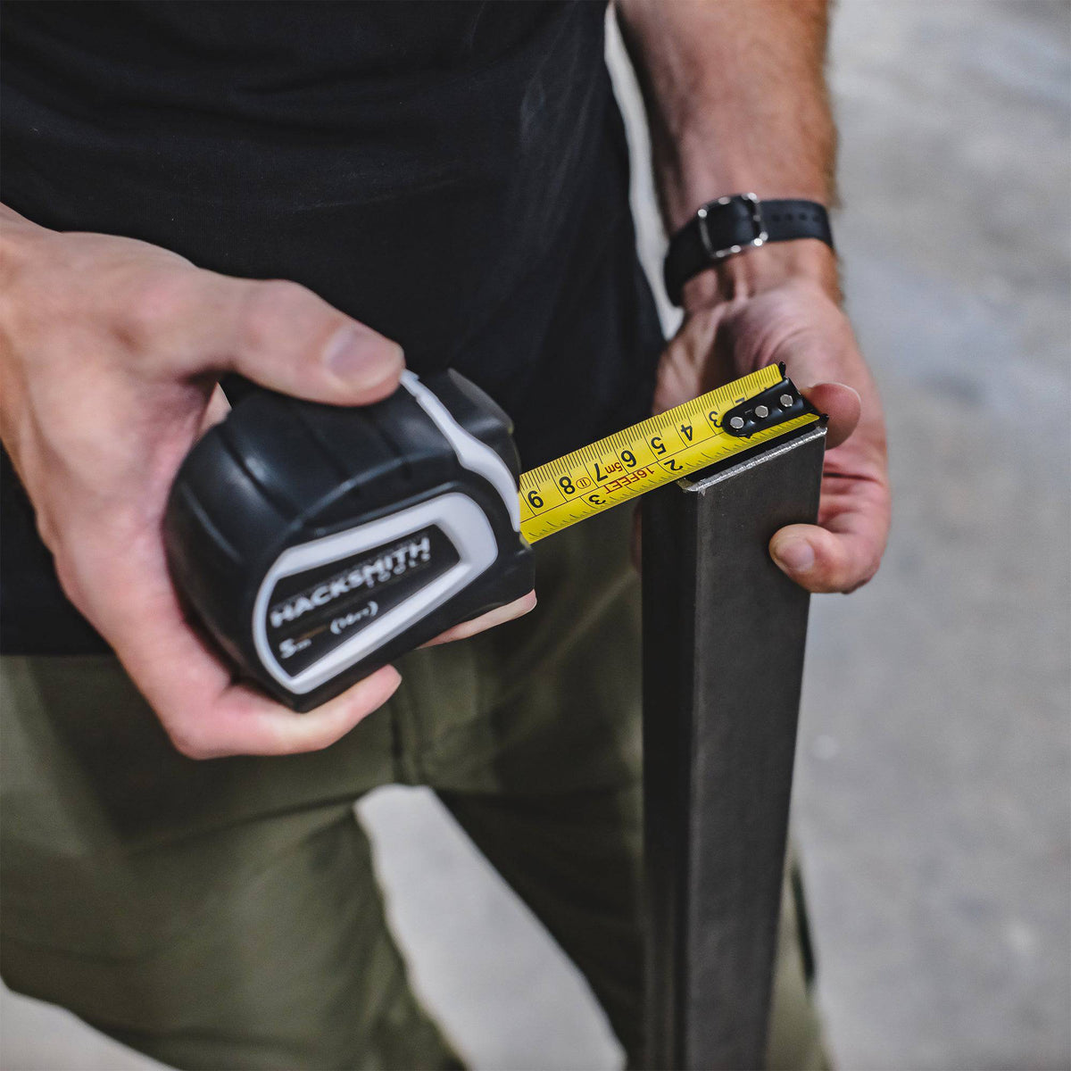 Hacksmith Tools tape measure with yellow and black casing, extended to show measurement markings on a measuring tape.